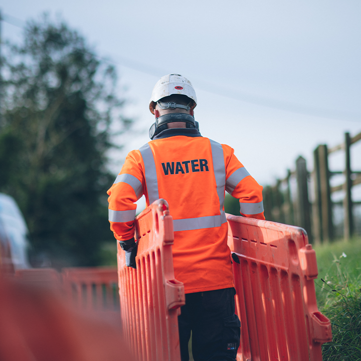 Wessex Water worker outside carrying road work barriers in hi vis